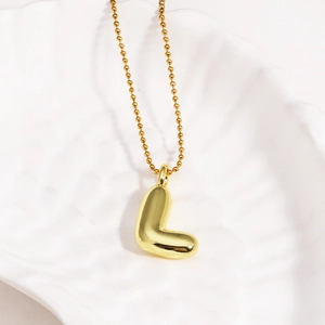 Detailed view of golden letter L bubble pendant on a bead chain over a shell plate