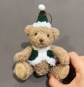 Detail of plush Christmas bear ornament with green knitted hat and scarf in hand