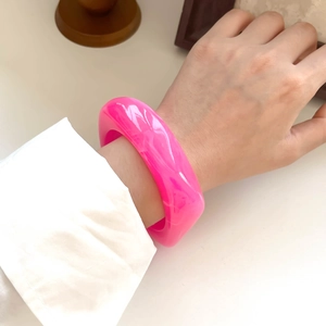 Close-up of a chunky fluorescent pink resin bangle bracelet worn on a female wrist