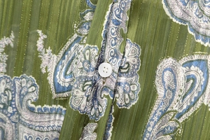 Macro detail of pleated green paisley fabric texture and white button on shirt