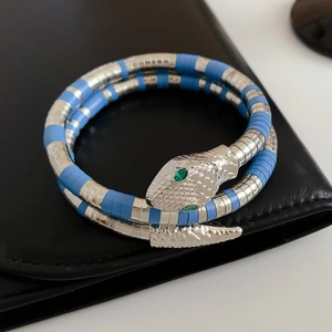 Macro detail of silver and blue coiled snake bracelet with vibrant green eyes