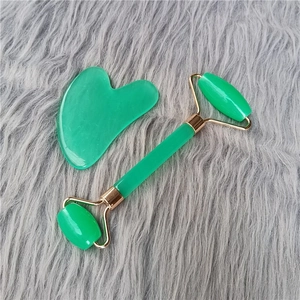 Macro view of green facial roller and heart-shaped gua sha tool on soft grey plush background