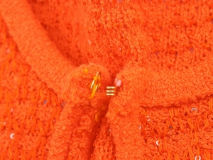 Detailansicht aus nächster Nähe: orangener Strick mit Pailletten und Metallhakenverschluss
