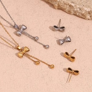 Detailed set of 18K gold and silver bow necklaces with matching stud earrings on stone