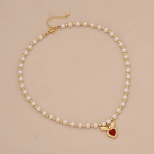 Macro detail of faux pearl necklace with a gold heart-shaped red pendant and leaf accent
