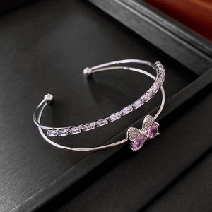 Close-up of silver double-layer open bangle with pink bow and rectangular zircon accents