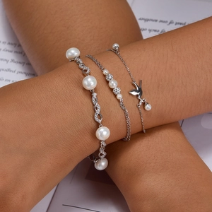 Detail of layered S925 silver bracelet featuring a bird charm and white pearls on wrist