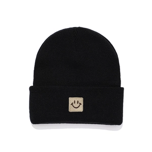 Close-up of a black knitted beanie featuring a beige square patch with a smiley face icon