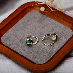 Elegant gold hoop earrings with emerald green square crystal on velvet display