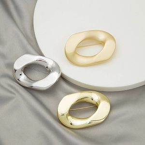 Close-up of three irregular geometric oval brooches in gold and silver on grey silk