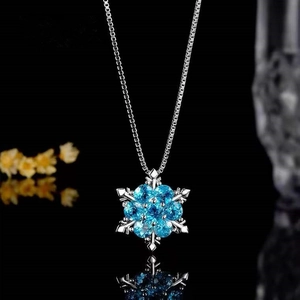 Snowflake necklace for kids with blue crystal pendant and silver chain on black surface