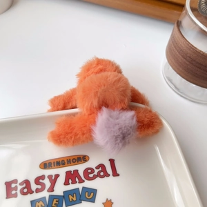 Close-up of fluffy orange and lilac plush hair claw clip on a white ceramic plate