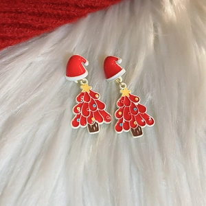 Detail of Christmas tree earrings with red enamel and yellow star on white plush background