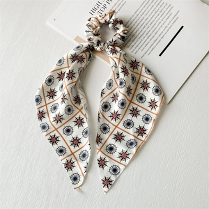 Detailed texture of cream bow scrunchie with orange grid and compass star patterns