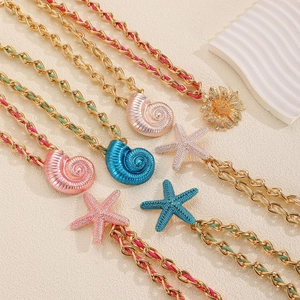 Close-up of golden chain necklace with colorful woven starfish and seashell pendants