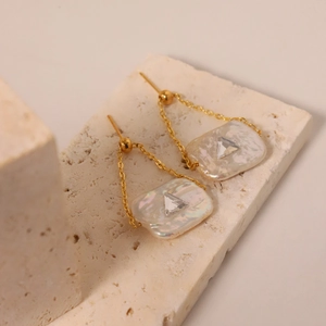 Detail of baroque pearl earrings with golden chain and rectangular shell pendant