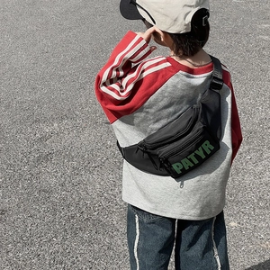 Kids black nylon fanny pack with green letter print shown on model in outdoor street style