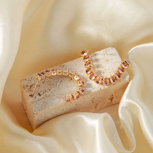 Elegant C-shaped gold-plated copper earrings with pink cubic zirconia on stone background