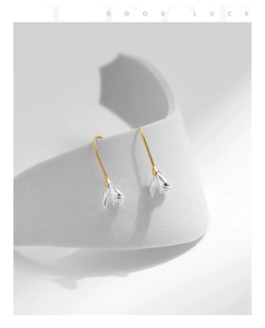Detail of silver magnolia flower drop earrings with gold hooks on a premium display