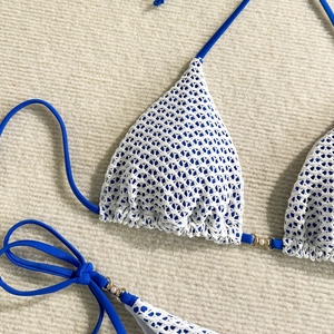 Detailed close-up of white crochet knit bikini with blue ties and pearl ring accents