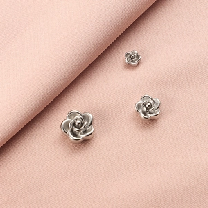Three 3D rose-shaped stainless steel beads in silver finish on pink fabric background