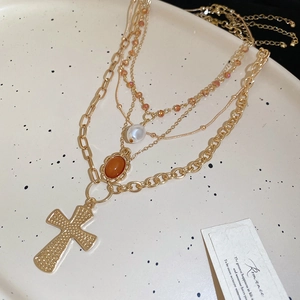 Detail of layered gold necklace with cross pendant pearl and amber resin stone on ceramic tray