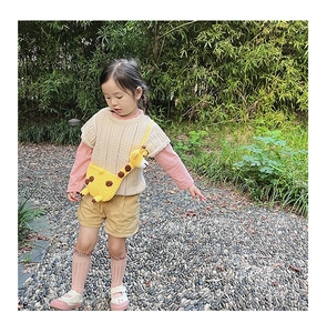 Detail of a handmade yellow knitted giraffe crossbody bag for kids in a natural bamboo setting