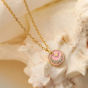 Collana donut in smalto rosa con stella e luna dorata su sfondo di conchiglia bianca