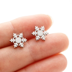 Macro shot of silver snowflake earrings on a fingertip showing the petite jewelry size