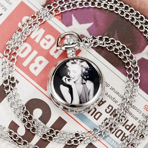 Macro shot of silver pocket watch featuring Marilyn Monroe portrait on newspaper background