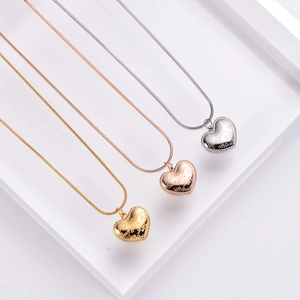 Three heart-shaped necklaces in gold, rose gold, and silver on an acrylic block