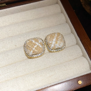 Detailed close-up of square fabric earrings with golden rhinestone borders on a velvet stand