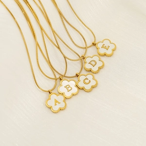 Detail of 18K gold-plated clover necklaces with white enamel and A-E letter pendants