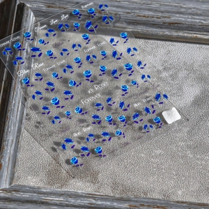 Macro detail of blue rose nail art stickers with metallic pearl finish and text