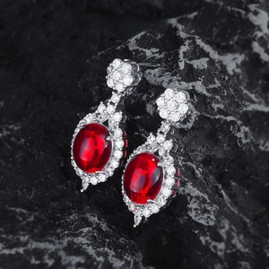 Macro detail of silver ruby earrings featuring oval red gemstones and white zircon halo