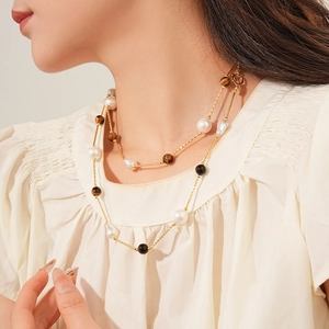 Detail of layered tiger eye and baroque pearl gold necklace on model neckline