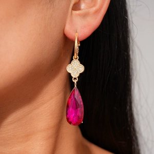 Close-up of rose red teardrop crystal earring with gold clover inlay on model's ear