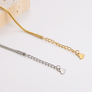 Snake chain bracelets with heart pendants in gold and silver finish on marble stone