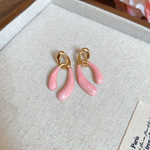Detail of elegant gold hoop earrings featuring light pink teardrop resin pendants on a tray