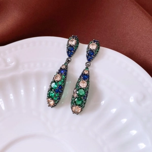 Detailed view of vintage teardrop earrings with colorful zircon stones on a ceramic plate