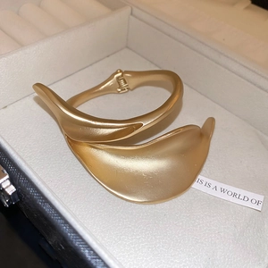 Detail view of a matte gold-finished leaf-shaped open cuff bracelet in a jewelry box
