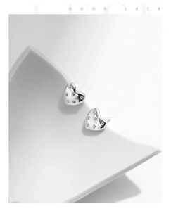 Macro view of S925 silver heart stud earrings with shimmering zircons on white surface