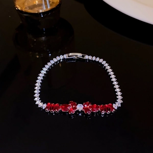 Close-up of elegant bracelet with red and clear leaf-shaped zircons on black background.