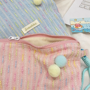 Detail der bunten Tweed-Textur mit rosa Reißverschluss und Plüsch-Bommel an der Handytasche