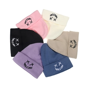 Flat lay of colorful knit beanies with stitched face embroidery on white background