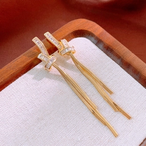 Detail of gold-plated knot tassel earrings featuring zircon stones on white fabric