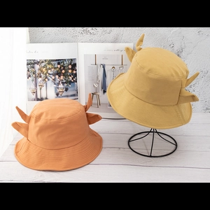 Detail of cow-horn bucket hats in orange and mustard yellow on a minimalist display