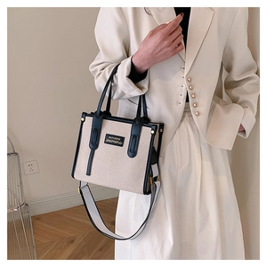 Model wearing a large canvas tote bag with black leather trim and wide shoulder strap