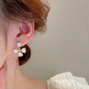 Détail de boucles d'oreilles trèfle en forme de cœur avec nacre et finition dorée