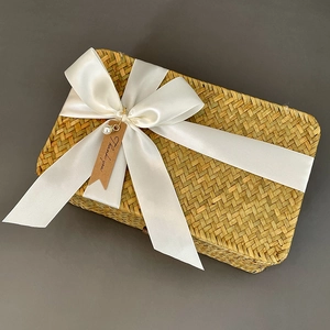 Detail of a rectangular seagrass gift box featuring a white satin ribbon and pearl tag